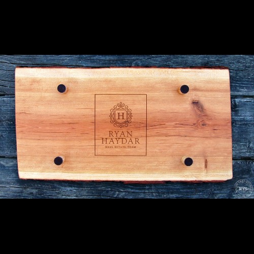 The back of a live edge charcuterie board showing a realtor logo engraved.