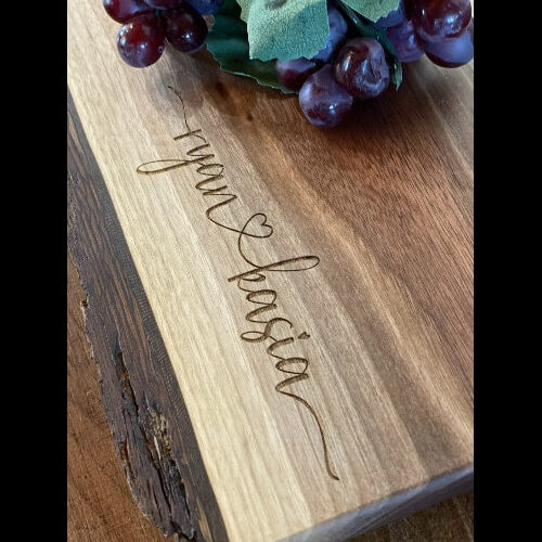An engraved walnut cheese board with two names connected with a heart.